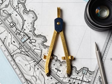 Top-down flatlay of a high-precision topographic map with brass dividers and technical drawing tools, bright daylight, sharp details
