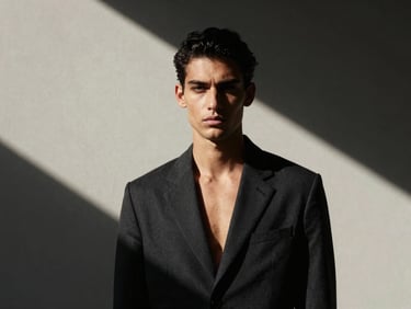 High-contrast portrait of a male model in direct sunlight with dramatic shadows, minimalist architectural setting.