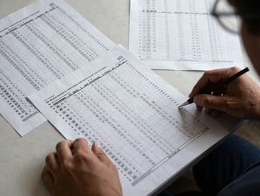 Close overhead view of election ballot papers spread on a table, hands sorting documents under natural daylight, institutional documentary style