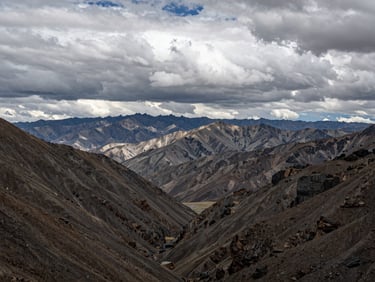 Wide environmental shot of the Wind River Range in overcast, dramatic light, low-contrast natural daylight with deep valleys and rocky peaks.