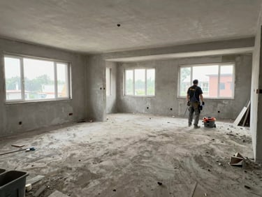 Wide shot of a freshly constructed interior room mid-cleaning: cement dust on floor, worker equipment visible but no people, construction debris partially cleared, documentary daylight through unfinished windows