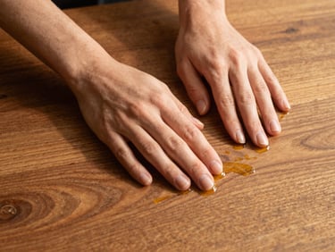 Warm editorial photography of hands applying natural oil to a rich walnut tabletop, highlighting the tactile organic grain, 35mm