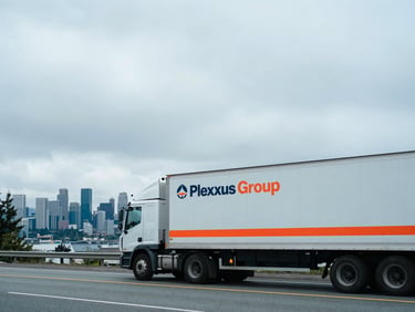 Wide environmental shot of a Plexxus Group truck on a highway near Seattle, with the city skyline in the distance, overcast Pacific Northwest daylight, cool tones, 35mm