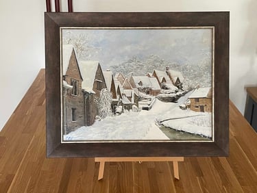 Framed oil painting of a snowy Cotswolds village with winter cottages and a frozen river.