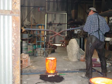 Positioning the tongs to lift the crucible of bronze for pouring