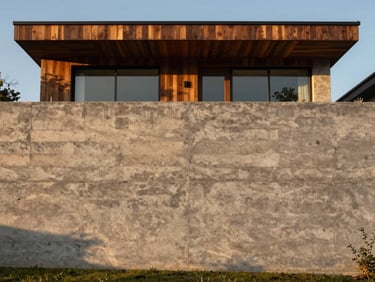 Straight-on architectural elevation of a massive board-formed concrete retaining wall framing a modern home, low-angle golden hour light casting deep timber-grain textures.