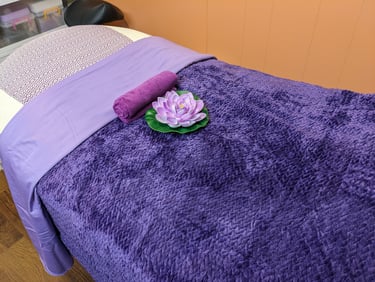 massage table with purple bedding and a lotus flower laying on top