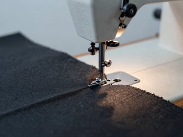 Macro close-up of industrial sewing machine stitching a heavy charcoal fabric roll, clean warm studio lighting, sharp textile textures, 35mm photography.