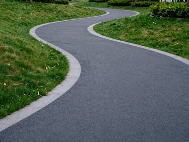 Wide architectural shot of a modern public park, charcoal grey rubber pathways integrating with natural green grass and concrete borders, soft daylight.