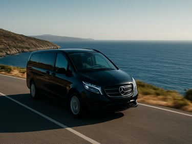 Wide scenic shot of a black luxury Vito driving smoothly along the Aegean coastal road, deep blue sea in the background, cinematic framing.