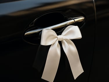 Close-up of a beautifully decorated luxury bridal car door handle, white silk ribbon, polished black metallic finish.