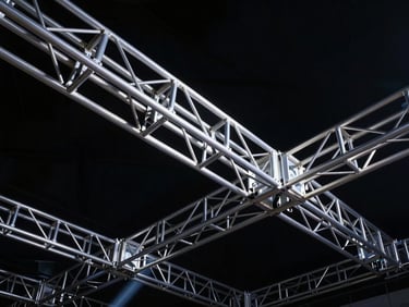Low-angle heroic shot of heavy-duty aluminum trussing and rigging structures, sharp industrial lines against deep shadows, crisp technical details, 35mm.