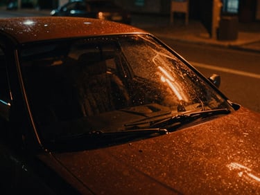 Cinematic film still, neon orange light reflecting on a wet car windshield, dark night street, rich shadows, 35mm anamorphic