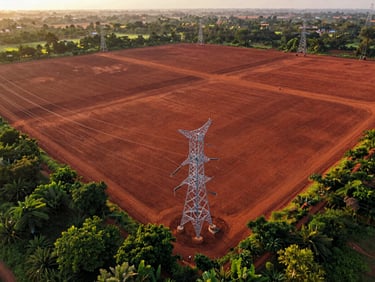 High-altitude drone photography of a vast, cleared red-soil land parcel in Karnataka, high-voltage transmission lines bordering the edge, low-sun golden hour, 35mm
