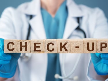 A doctor in a white lab coat holds wooden blocks spelling check-up for a medical exam.