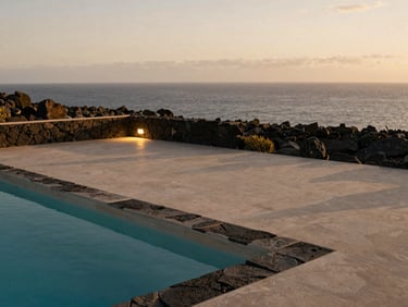 A minimalist outdoor pool terrace with volcanic stone details, overlooking Tenerife's coast at soft dusk, warm side-lighting.