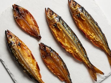 Overhead flat-lay of smoked fish fillets arranged on white slate under cool diffused studio lighting, deep amber colour of flesh visible, no warmth in light, clean precise framing