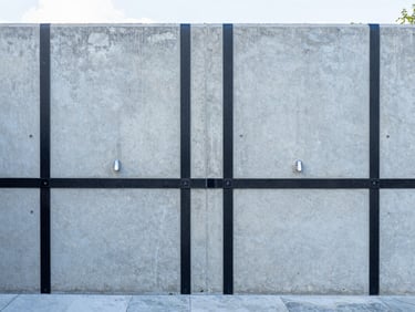 Straight-on architectural photograph of a clean concrete basement wall with neat carbon fiber reinforcement straps installed vertically, bright utility lighting, cool slate tones, 35mm.