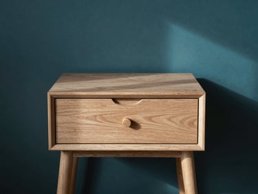 Studio shot of a minimalist wooden bedside table with one drawer, warm daylight, elegant shadow play, architectural interior style