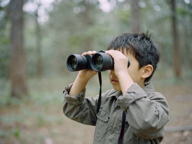Candid portrait of a young child looking through binoculars in a forest glade, natural overcast light
