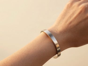 Macro shot of a minimalist stainless steel bracelet on a woman's wrist, warm golden hour sunlight, cream background.