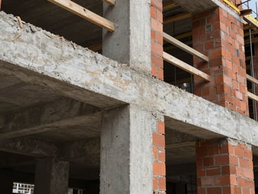 Raw structural masonry on an active construction site, exposed concrete beams and red brick walls, high-contrast natural light.