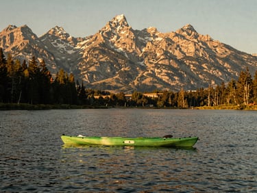 A single green kayak floating on the calm Teton River during a warm, golden summer afternoon.