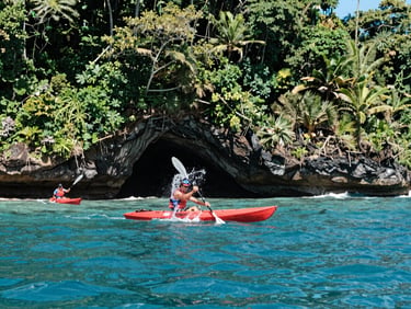 Dynamic shot of two red kayaks paddling near dramatic ocean caverns in Uvita, splashing water, bright coastal daylight