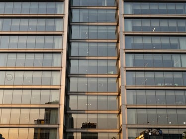 Symmetrical architectural elevation of DLF The Camellias glass facade reflecting warm golden-hour light, modern structural geometry.