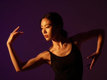 Low-key dramatic portrait of a female dance instructor with dark hair, warm tungsten side-lighting, elegant posture, deep amethyst background.