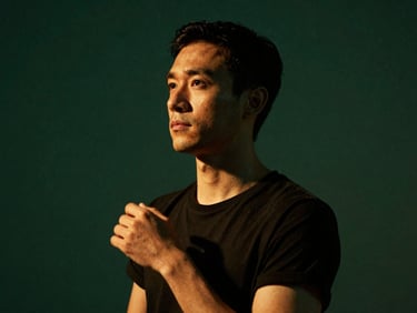 Low-key dramatic portrait of a male dance instructor, warm lighting, thoughtful expression, deep emerald background.