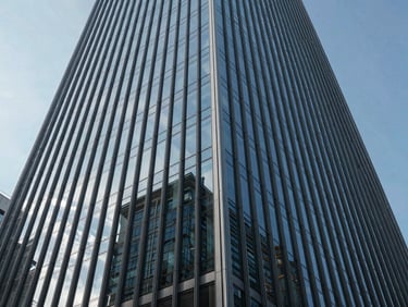 Low angle shot of a modern glass skyscraper reflecting a clear sky, sharp linear shadows, architectural geometry.