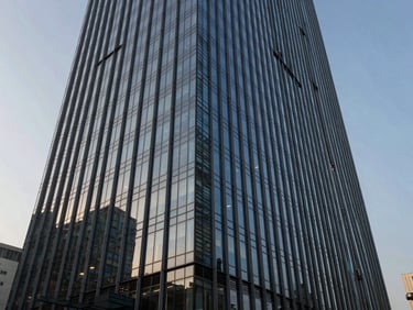 A wide-angle, crisp architectural shot of a modern glass skyscraper in Mumbai against a cool morning sky, sharp geometric shadows casting across the facade.