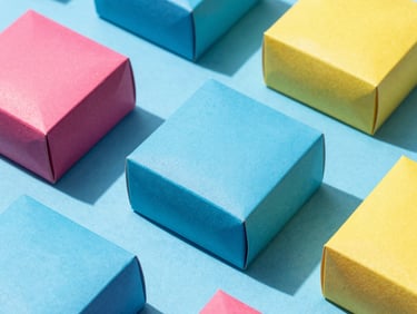 High-angle flat lay of vibrant modern gift boxes on a bright blue surface, crisp direct sunlight casting sharp shadows.