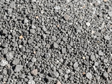 Macro shot of fine crushed stone seal aggregate, uniform small grey particles.