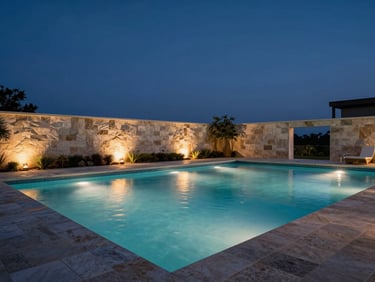 Luxury outdoor swimming pool at blue hour, still water reflecting warm uplighting along pool walls, stone coping edged with precise landscaping, no people — wide environmental frame with deep navy sky above