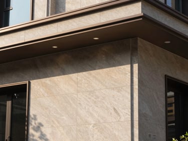 Close-up architectural detail of a luxury residential façade — polished stone cladding, recessed linear lighting, deep shadow reveals, natural daylight raking across the surface from the left, conveying precision and material quality