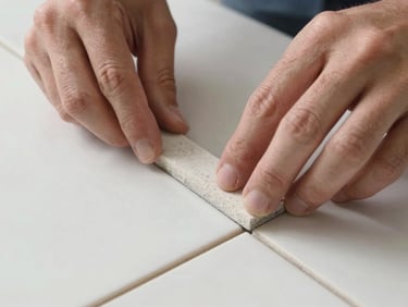 Macro close-up of a tiler placing a spacer between two large porcelain tiles, showing perfect alignment and clean hands, bright natural daylight.