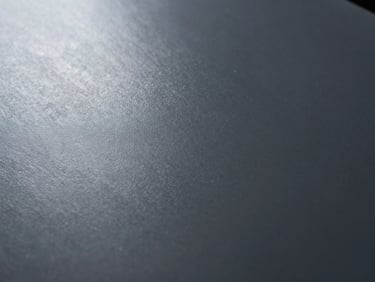 Macro shot of a matte deep slate gray coated metal surface, smooth texture, soft diffuse lighting