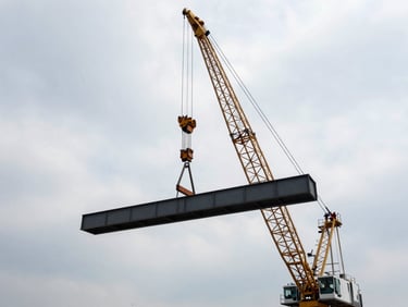 Wide environmental shot of a massive mobile crane lifting a structural steel beam against an overcast industrial sky