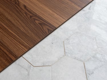 Extreme close-up overhead shot of a flush transition between rich walnut hardwood planks and clean hexagonal marble tile, showing perfect alignment and crisp grout lines in natural daylight.