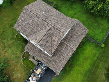 Aerial view of a residential home with newly installed asphalt shingle roofing and a debris dumpster.