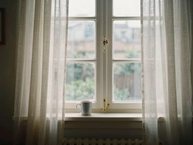 An early 2000s digital photograph of a living room window, morning light coming through thin curtains, a coffee mug on the sill, slightly flat digital color rendering, no grain