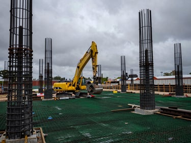Maquinaria de perforación de cimentaciones profundas en acción en un sitio de construcción, con armados de acero expuestos, bajo luz natural de día nublado, ángulo contrapicado.