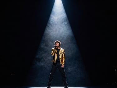 High-contrast film still of a musical artist performing under a single dramatic spotlight on a dark, textured soundstage, haze in the air.