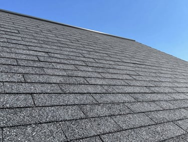 Close-up of newly installed architectural asphalt shingles in a charcoal gray, showing clean lines and precise layering, bright daylight.