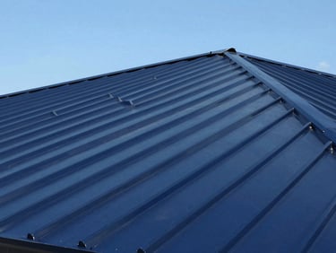 Detail shot of a standing seam metal roof in a deep navy color, showing crisp, interlocking panels and a smooth finish, under a clear sky.
