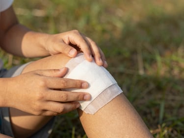 Close-up of hands applying a bandage to a child's knee, in a warm, natural light setting, showing care and practical action, soft focus background, 35mm lens.