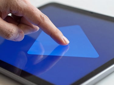 Macro shot of a finger tapping a vibrant blue geometric shape on an Android tablet screen.