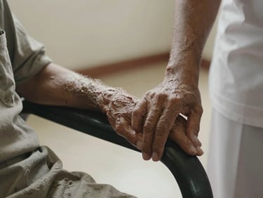 A caregiver's hand resting gently beside an elderly resident's hand on a chair armrest, soft diffused Kerala afternoon light, worn fabric visible, intimate and unhurried